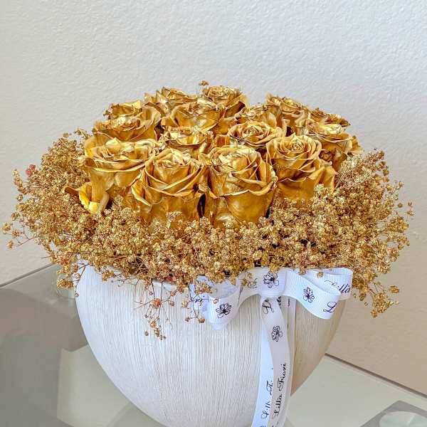 Gold roses in a white textured vase with a white ribbon