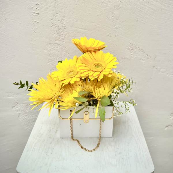 Yellow gerbera daisies in a white box with a gold chain handle