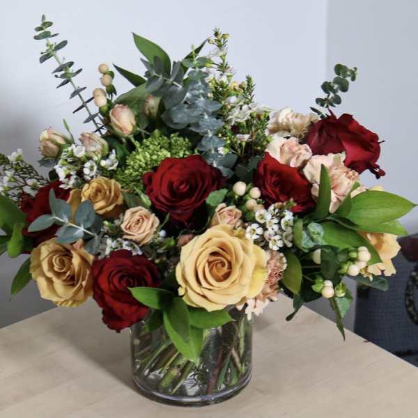 Mixed roses in a clear glass vase with greenery and small white filler flowers