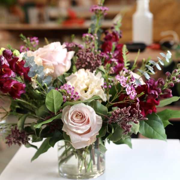 Mixed bouquet of pale pink roses and burgundy flowers in a glass vase