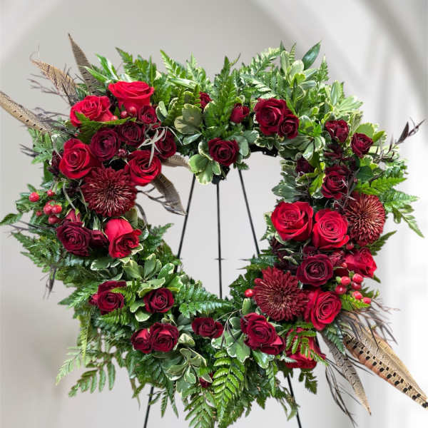 Heart-shaped floral wreath with red roses and greenery on a stand