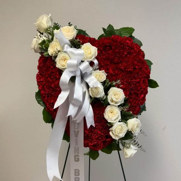 Heart-shaped red floral wreath with white roses and a white ribbon on a stand