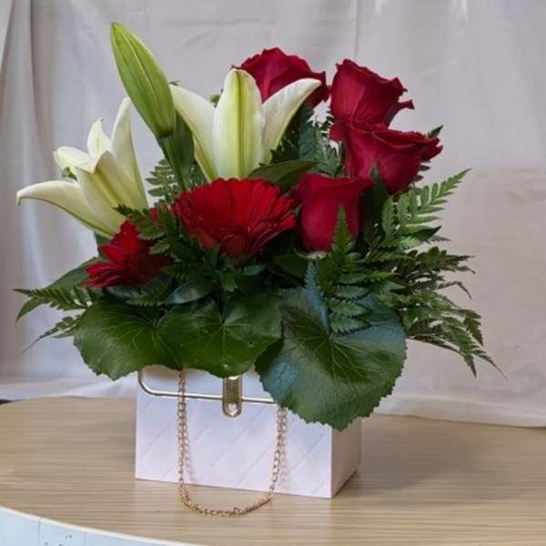 Red roses and white lilies arranged in a white gift bag