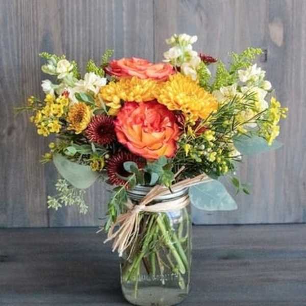 Mixed bouquet of orange, yellow, and white flowers in a glass jar