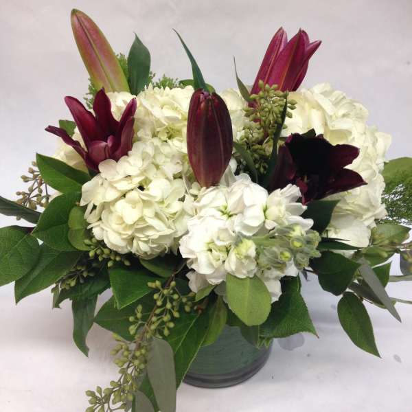White hydrangeas with burgundy lilies in a glass vase