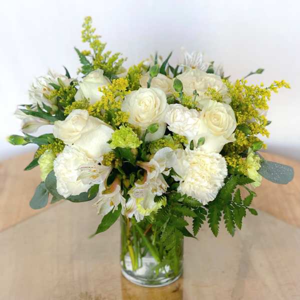 White roses and carnations in a clear glass vase with yellow filler flowers