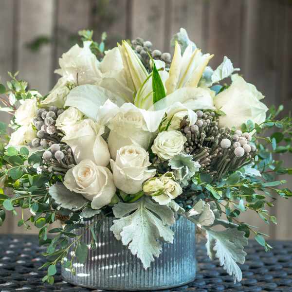 White roses and lilies arranged in a ribbed silver vase