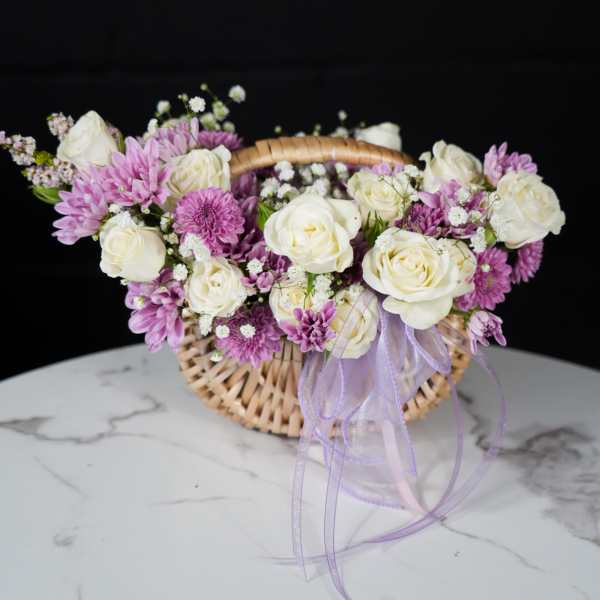 Basket arrangement of white roses and purple daisies with a lavender ribbon