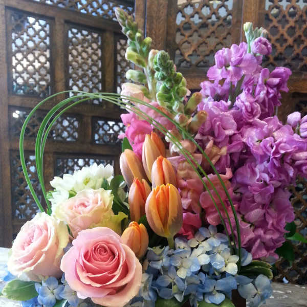 Mixed bouquet of pink roses, orange tulips, and purple blooms in a dark container