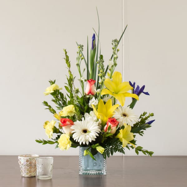 Mixed bouquet in a square glass vase with yellow lilies, white daisies, and roses