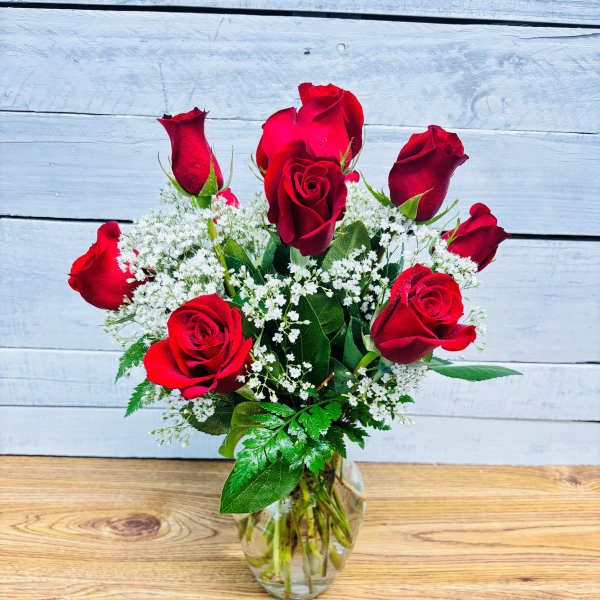 Red roses arranged in a clear glass vase with white filler flowers