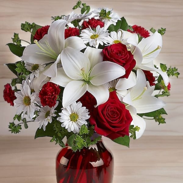 Bouquet of red roses, white lilies, and daisies in a red glass vase