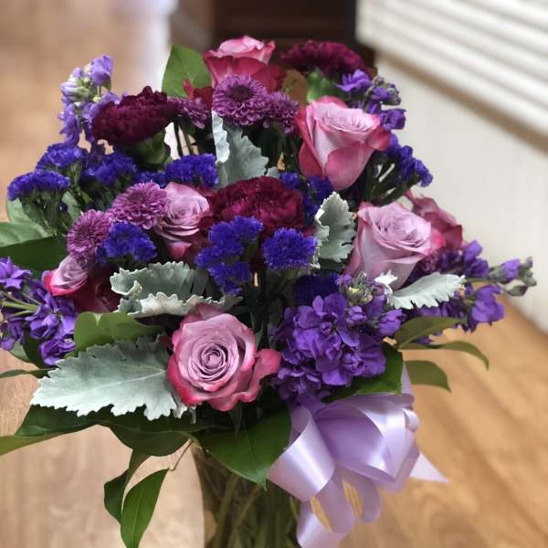 Bouquet of pink and purple flowers in a glass vase with a lavender ribbon