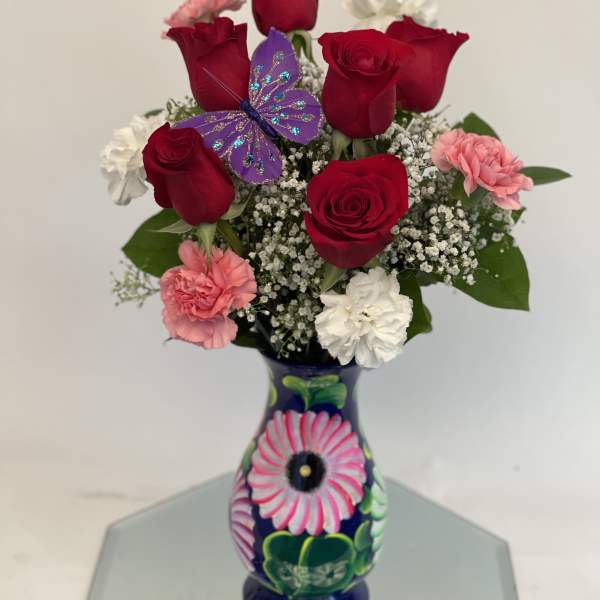 Red roses and pink carnations in a painted vase with a purple butterfly decoration