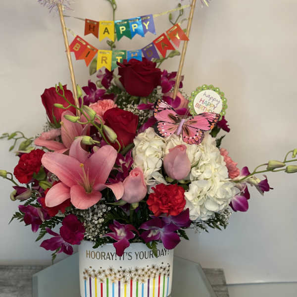Birthday flower arrangement with roses, lilies, and hydrangeas in a decorated container