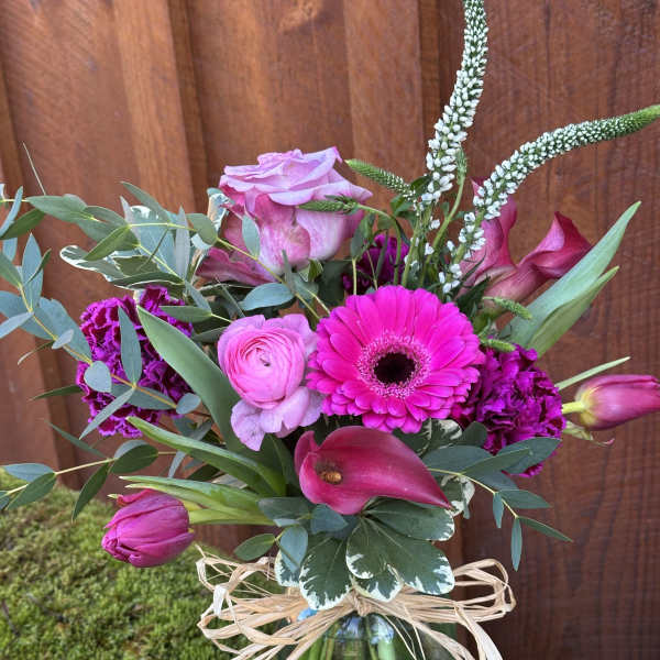 Pink and magenta bouquet in a blue glass vase with raffia bow