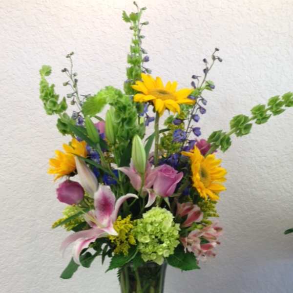 Tall mixed bouquet in a glass vase with sunflowers, lilies, and roses