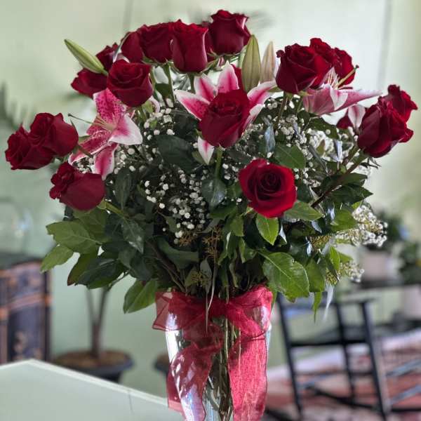 Red roses and pink lilies in a clear glass vase with a red ribbon