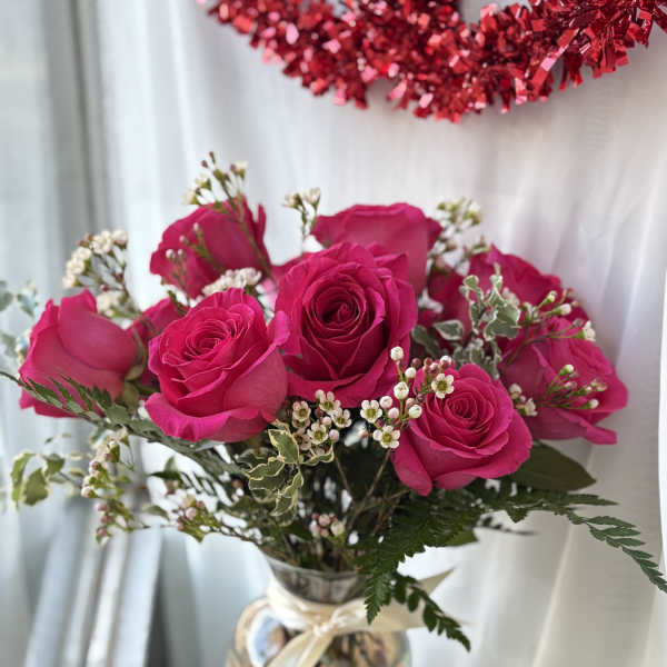 Arrangement of hot pink roses with small white filler flowers in a clear glass vase with a ribbon bow