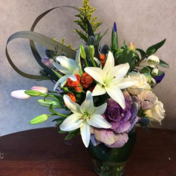 Mixed bouquet with white lilies and purple blooms in a glass vase