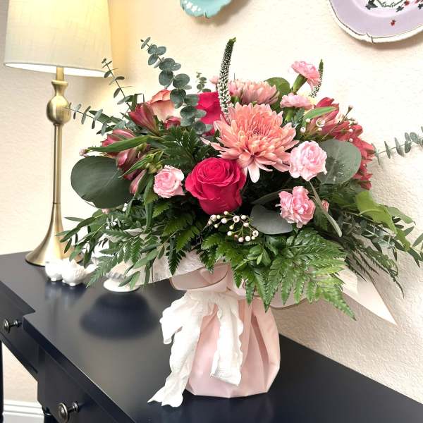 Pink and red mixed flower arrangement in a wrapped vase