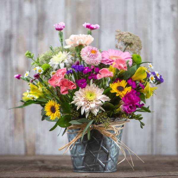 Mixed bouquet of colorful flowers in a metal vase with a raffia bow