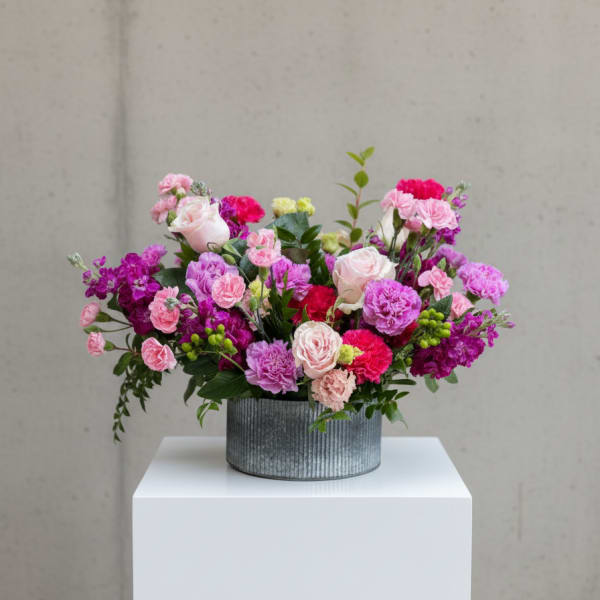 Low arrangement of pink, purple, and red roses and carnations in a round metal container