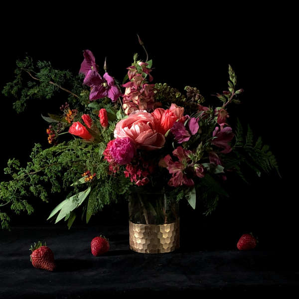 Mixed bouquet in a gold textured vase with strawberries on a dark surface