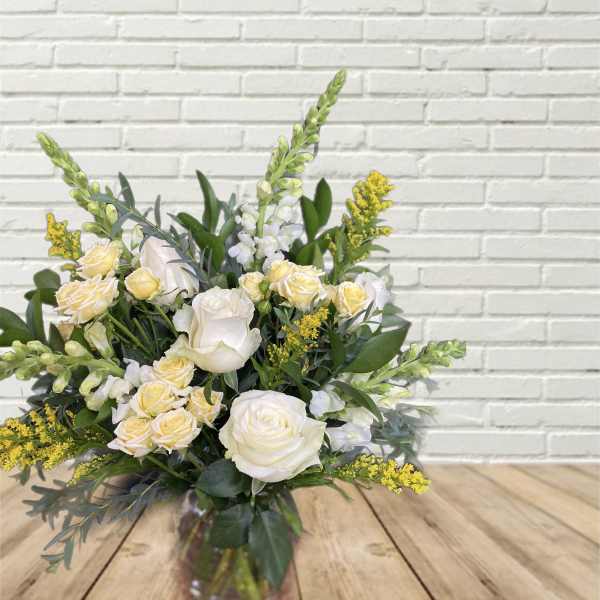 White and pale yellow roses in a glass vase with yellow filler flowers