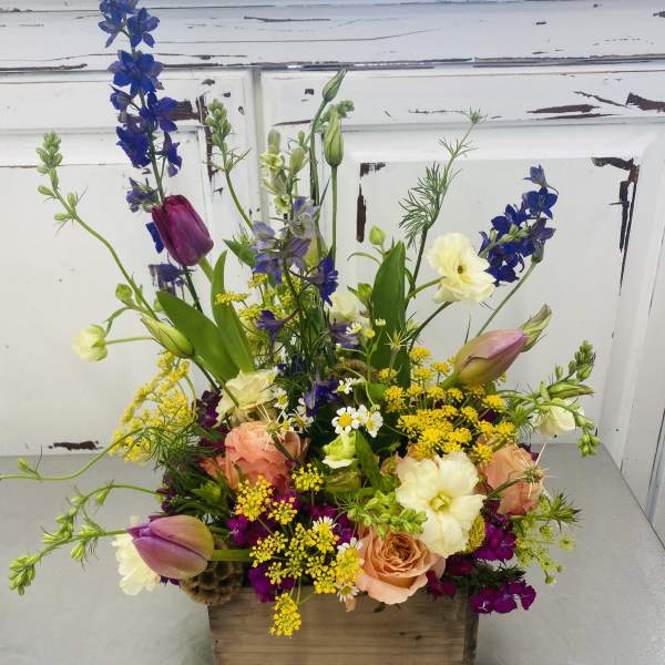 Mixed bouquet in a wooden box with tulips, roses, and blue delphinium