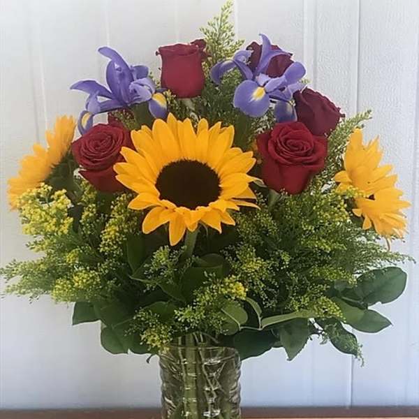 Bouquet of sunflowers, red roses, and purple irises in a glass vase