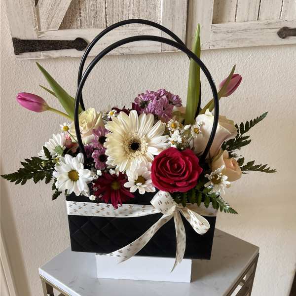 Mixed arrangement of roses, gerbera daisies, tulips and mums in a black handbag-style box with ribbon bow