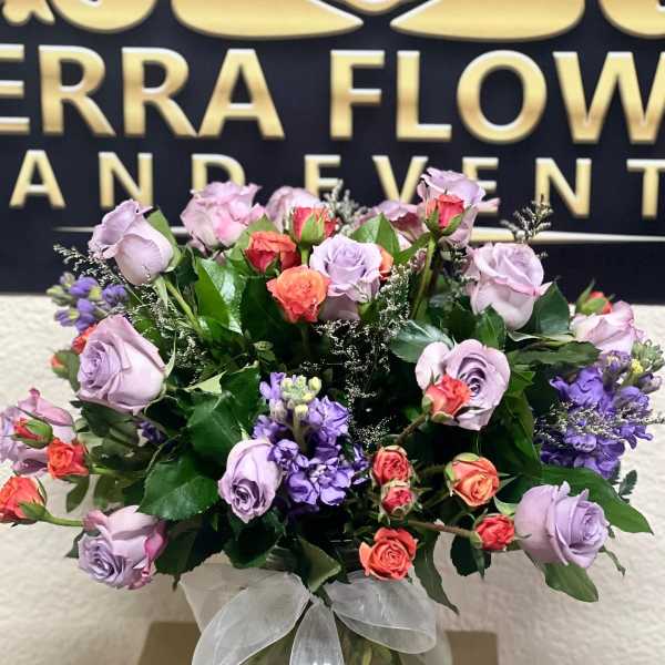 Lavender and coral roses in a round glass vase with a white ribbon