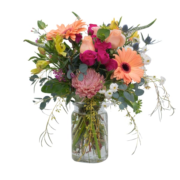 Mixed bouquet of peach gerbera daisies, pink roses, and assorted blooms in a clear glass jar vase
