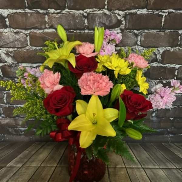 Bouquet of red roses, yellow lilies, and pink carnations in a red vase