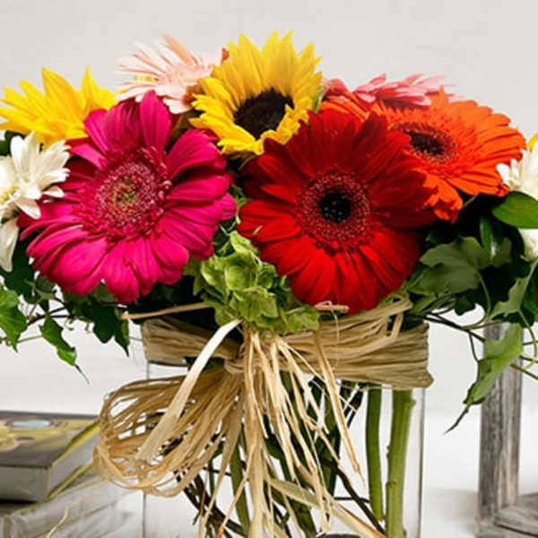 Bright gerbera daisies arranged in a clear square vase with raffia ribbon