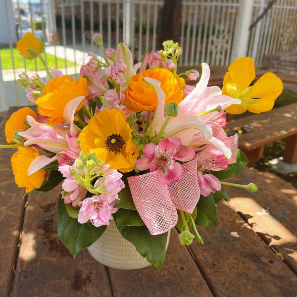 Bouquet of orange and pink flowers in a white vase with a pink ribbon