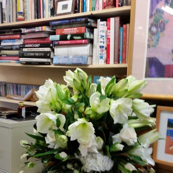 White lilies arranged in a tall white vase on a desk