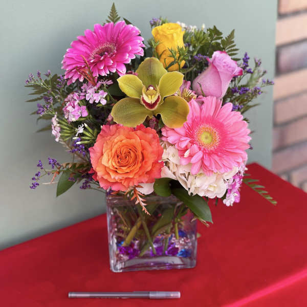 Mixed bouquet in a square glass vase with pink, orange, yellow, and white blooms