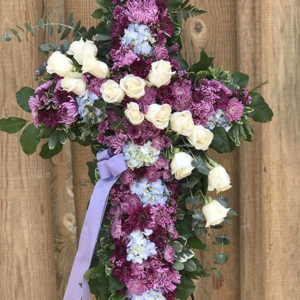Cross-shaped floral tribute with white roses and purple blooms