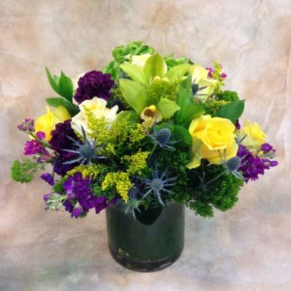 Mixed bouquet of yellow, purple, white, and green flowers in a dark vase