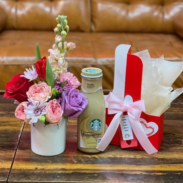 Small flower arrangement with a gift bottle and wrapped box on a table