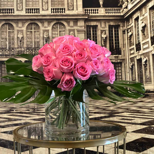 Pink rose bouquet in a clear glass vase with large tropical leaves