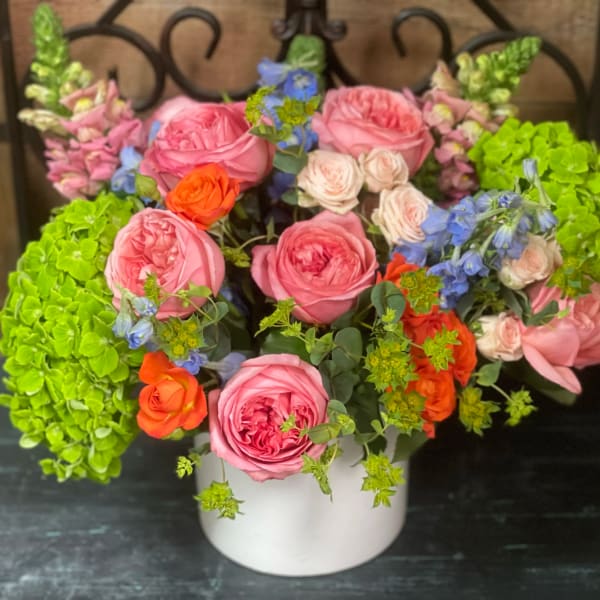 Pink and orange roses with blue flowers in a white vase