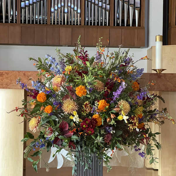 Large mixed floral arrangement in a tall vase with orange, purple, red, and white blooms