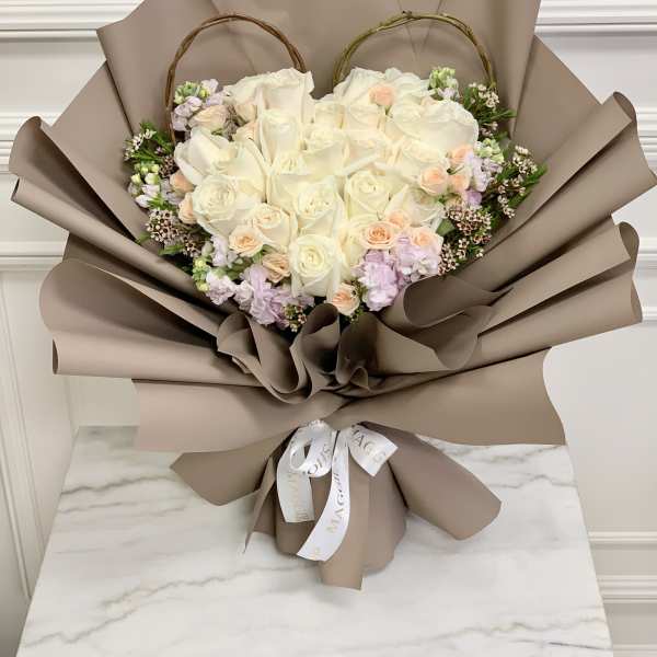 Heart-shaped bouquet of white and blush roses wrapped in taupe paper