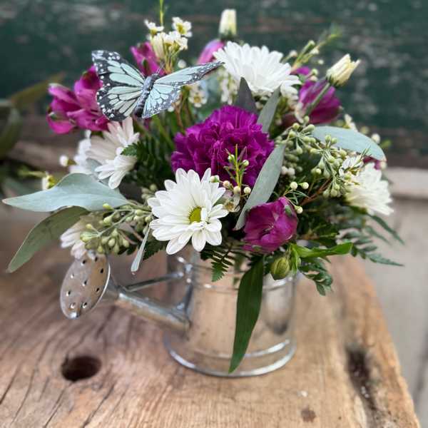 Bouquet of white daisies and magenta flowers in a clear glass mug with a butterfly decoration
