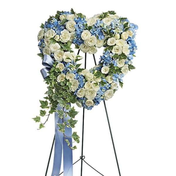Heart-shaped floral wreath of white roses and blue flowers on a stand