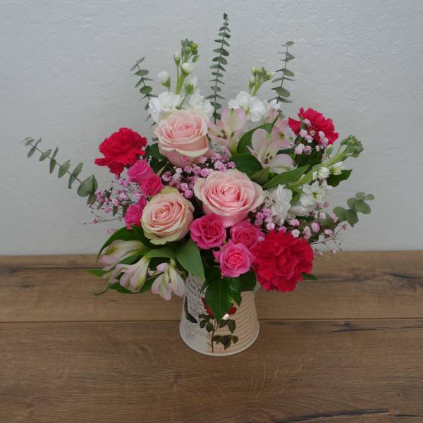 Pink and red mixed flower arrangement in a decorative tin container