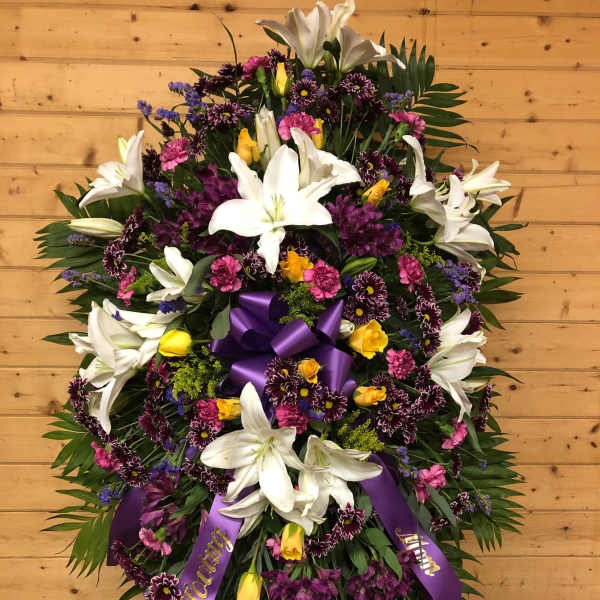 Large standing floral spray with white lilies, purple and pink flowers, and a purple ribbon